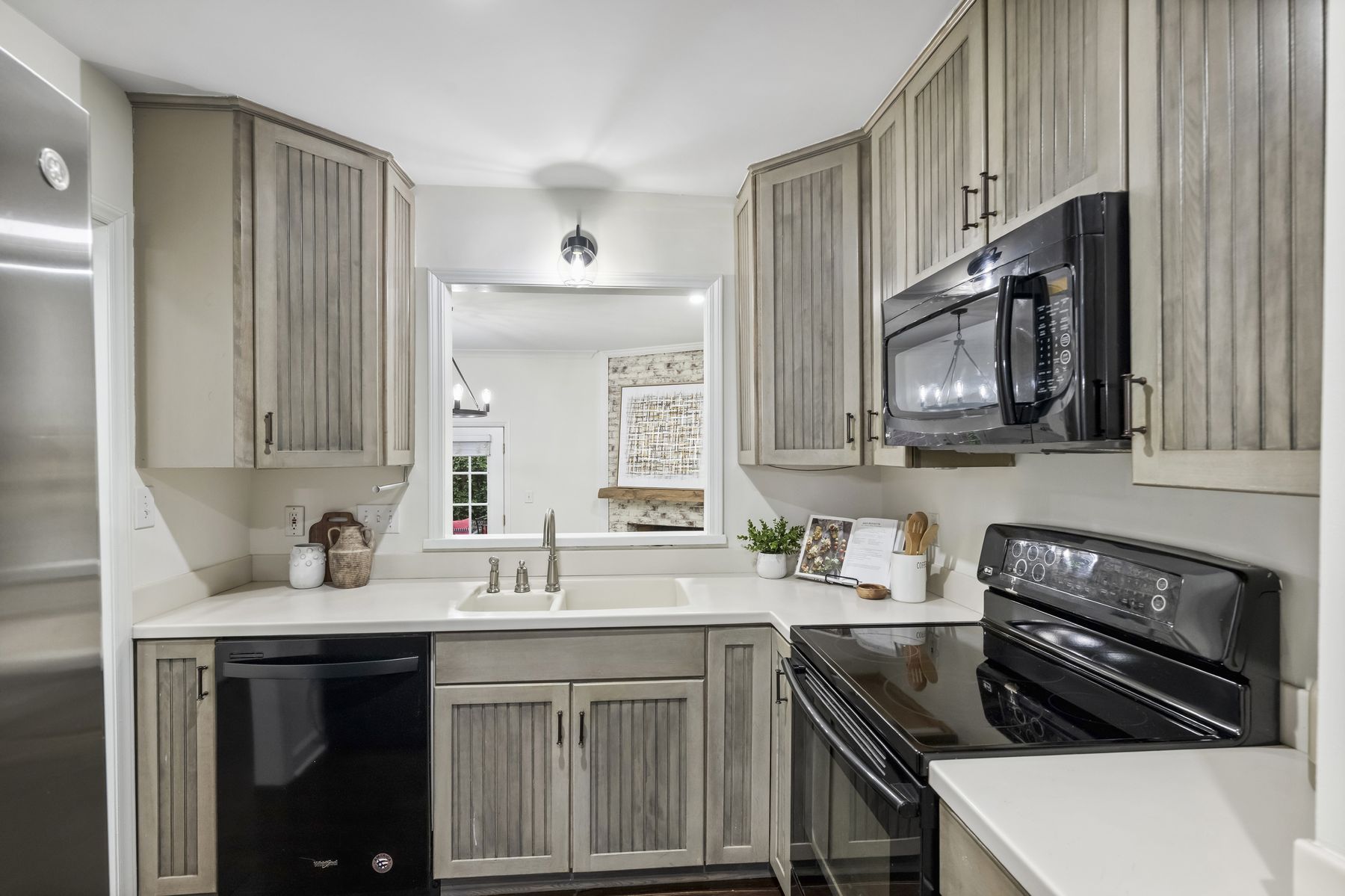 Kitchen with greige cabinetry, quartz counters, and a pass-through window to the living room